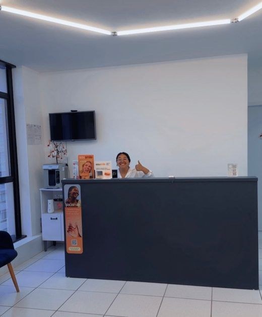 Recepção da clínica pronta, com balcão escuro, televisão na parede e uma atendente sorrindo.