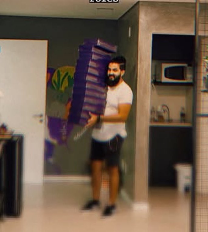 Lucas carregando uma pilha de caixas roxas, no dia de montar o estúdio.
